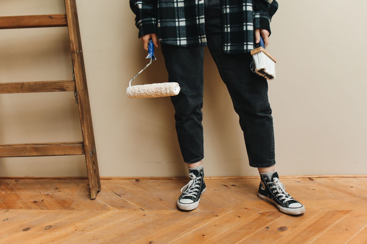 about-002 A person holding a paint roller and brush while carrying out a home renovation project.